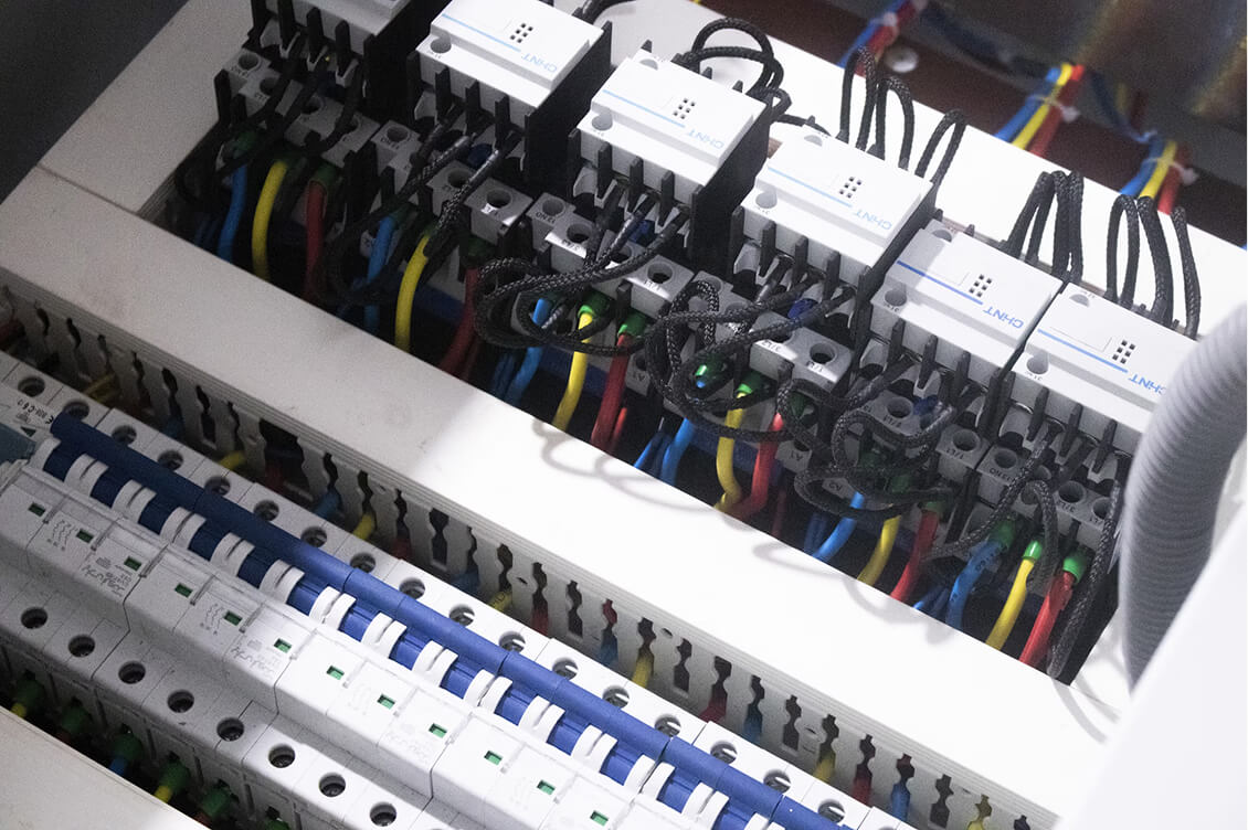 Close-up of an electrical distribution board with multiple circuit breakers and neatly organized colored wiring.