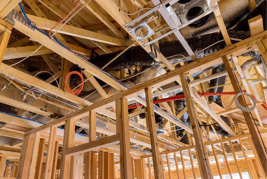 Exposed wooden framing with electrical wiring and ductwork installation in progress during commercial building construction.